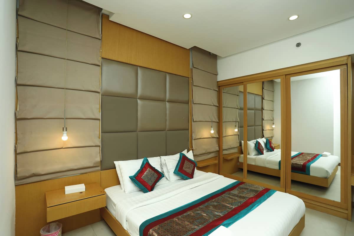 A modern hotel room with a large bed, a wooden nightstand, a mirror, and a headboard with a padded design.