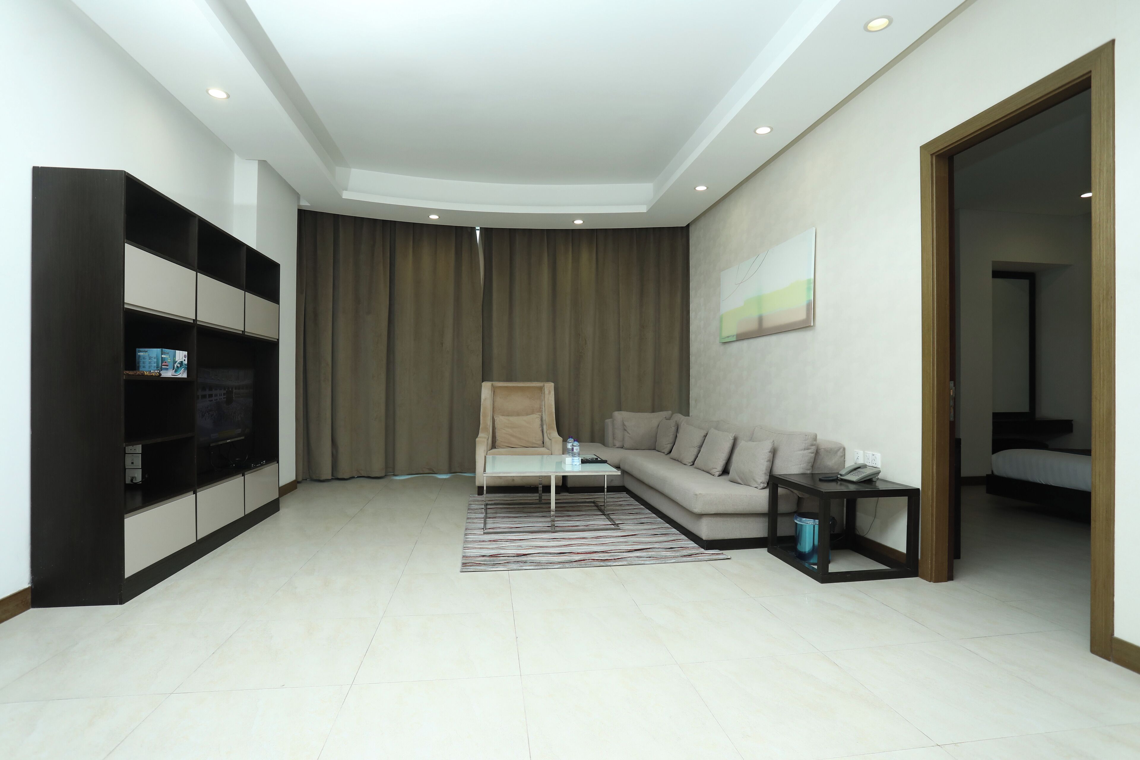 A modern living room with a sofa, a coffee table, a TV on a stand, and a large window with curtains.