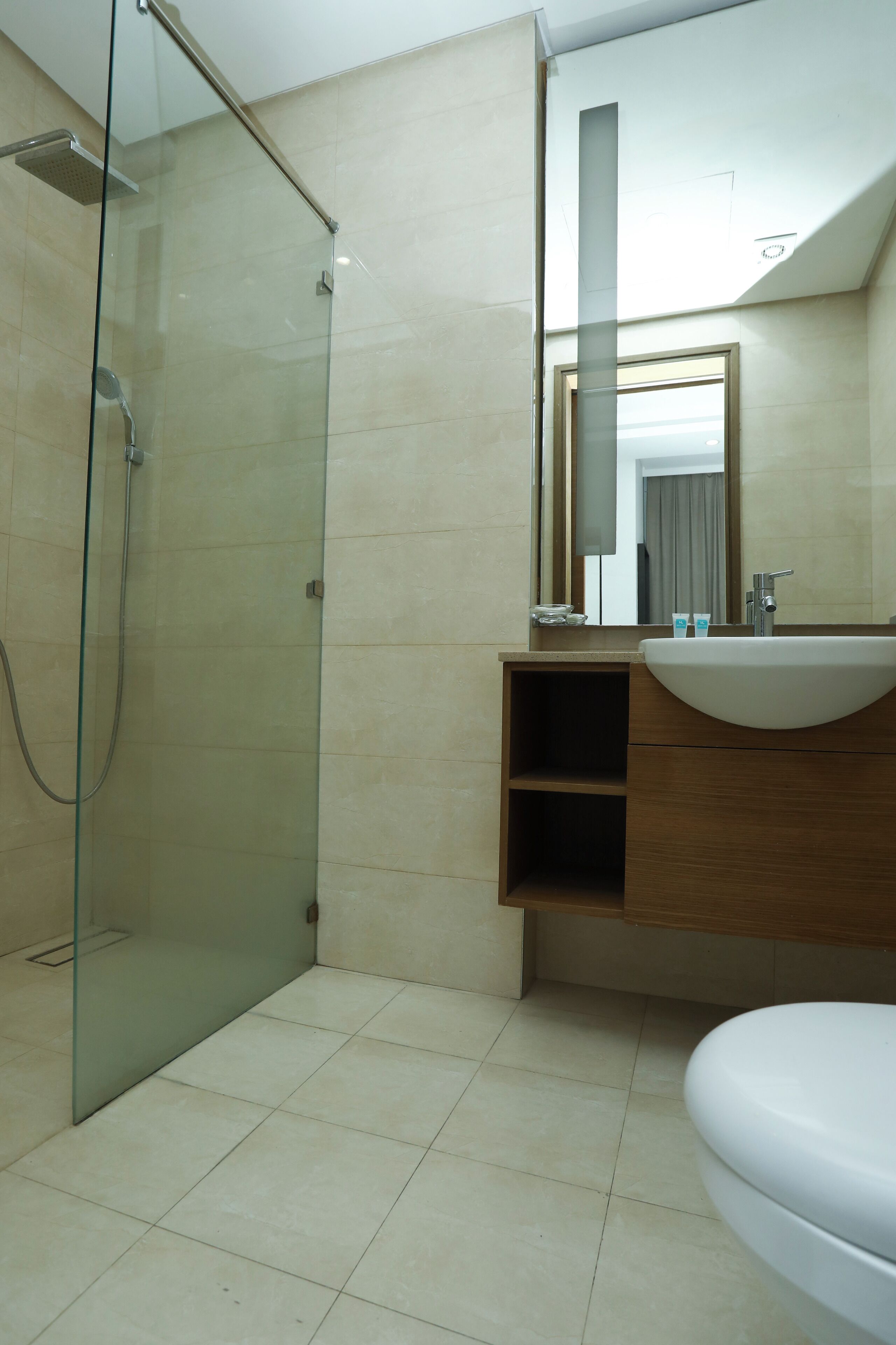 Un baño moderno con ducha de vidrio, tocador de madera con lavamanos y un espejo grande.
