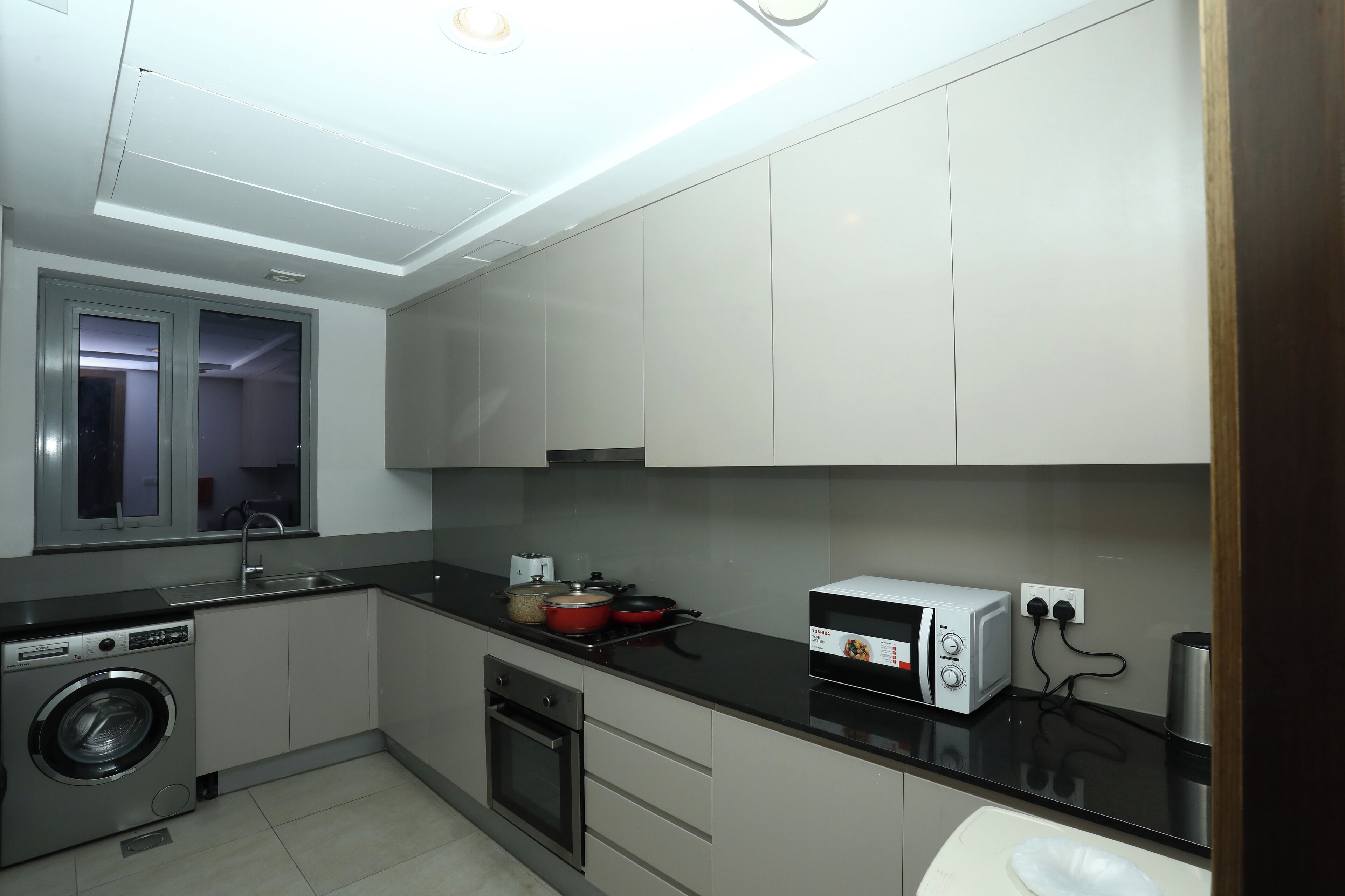 A modern kitchen with a washing machine, oven, microwave, and a window.