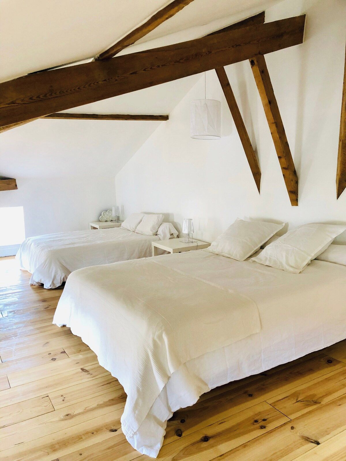 Una habitación con dos camas, vigas de madera, un colgante de luz y una mesita de noche blanca con lámpara.