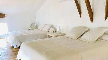 Una habitación con dos camas, vigas de madera, un colgante de luz y una mesita de noche blanca con lámpara.