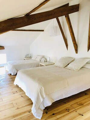 Una habitación con dos camas, vigas de madera, un colgante de luz y una mesita de noche blanca con lámpara.