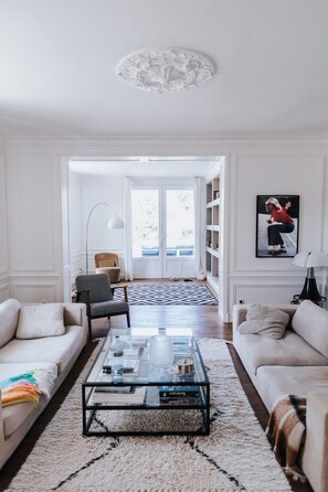 A modern living room with a glass coffee table, two sofas, a patterned rug, and a bookshelf.