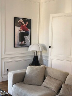 Een kamer met een bank, een lamp, een lijst aan de muur en een deur.