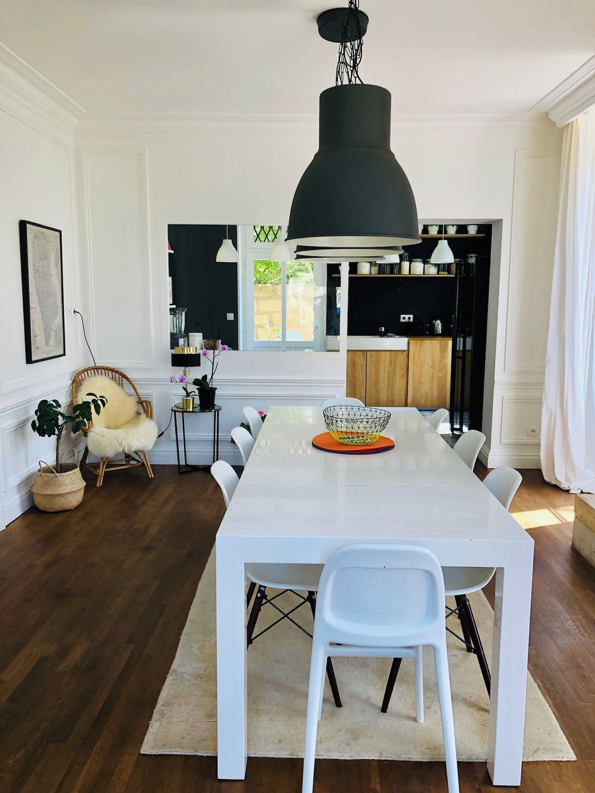 Un comedor moderno con una mesa blanca, lámparas colgantes negras y vistas a la cocina.