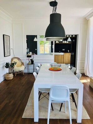 Un comedor moderno con una mesa blanca, lámparas colgantes negras y vistas a la cocina.