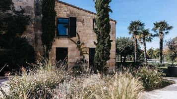 Un edificio de piedra con una ventana y una puerta, rodeado de árboles altos y un jardín cuidado.