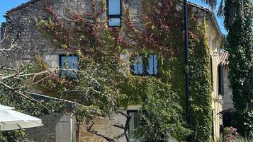 Un edificio de piedra con techo inclinado, una ventana pequeña y un árbol en primer plano.