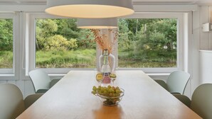 En matplats med ett långt bord, stolar, en hängande lampa, en vas med torkade växter och en skål med frukt.