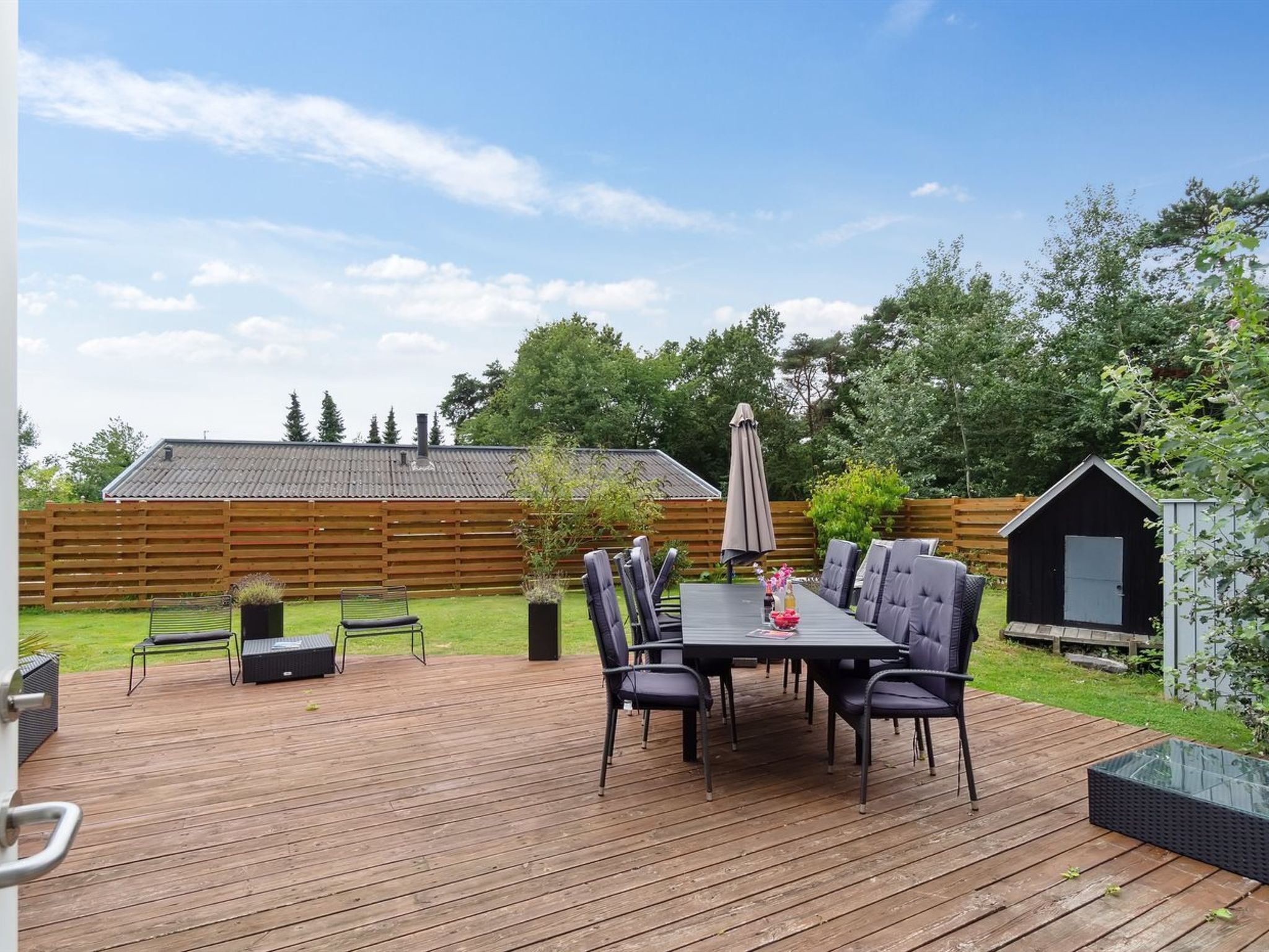 A wooden deck with a table and chairs, surrounded by a wooden fence and a shed.