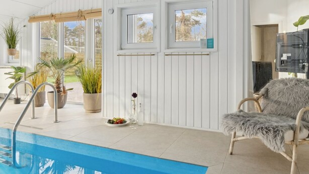 Ett poolområde med en blå pool, vita väggar och en fåtölj i rotting.