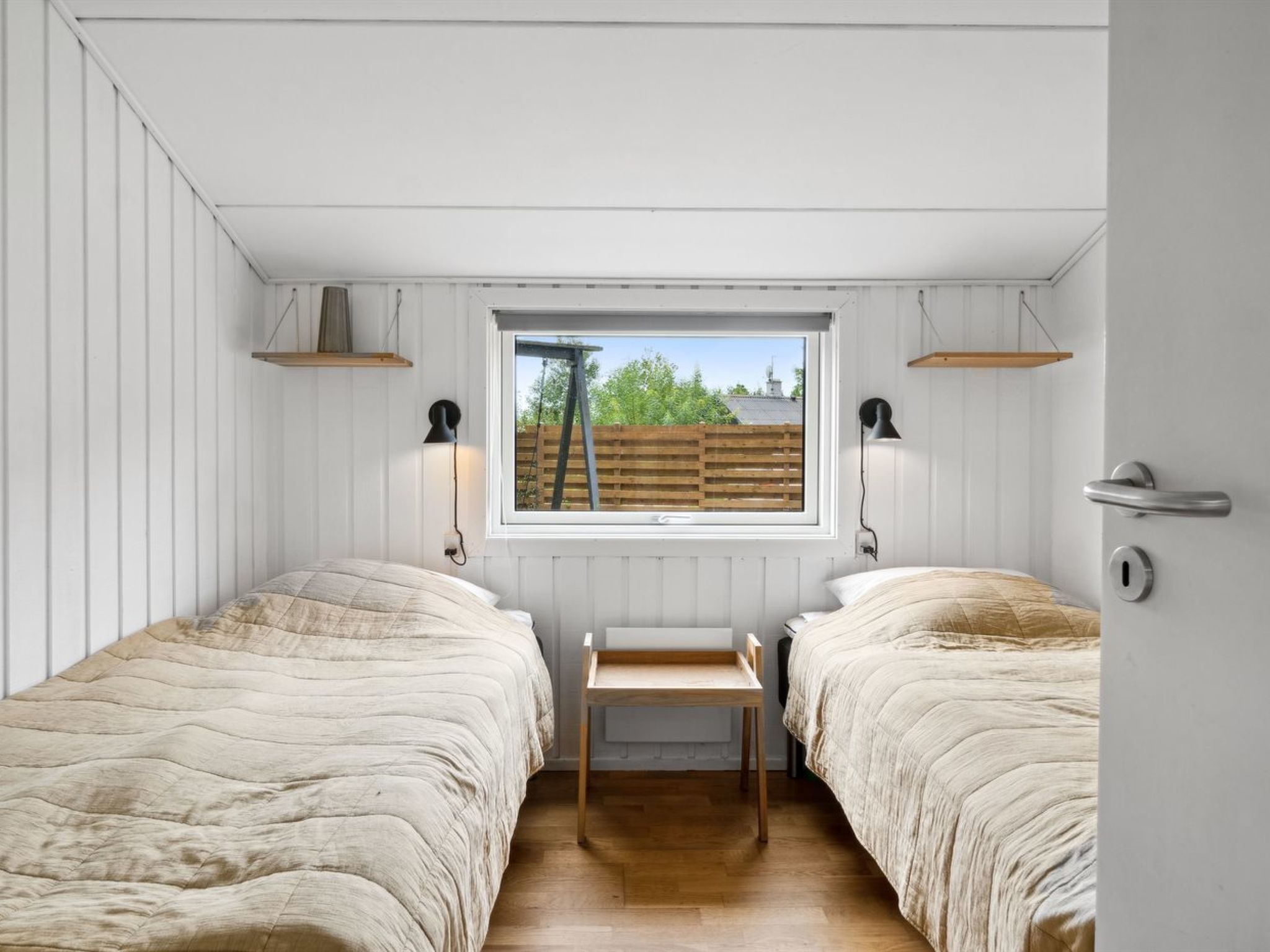 A bedroom with two beds, a window, and a small table.