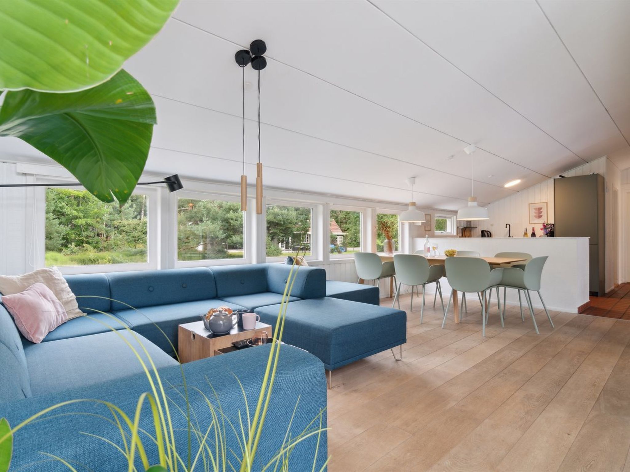A modern living room with a blue sofa, a dining area with chairs, and a kitchen in the background.