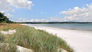 En strand med vit sand, klarblå himmel och avlägsna kullar.