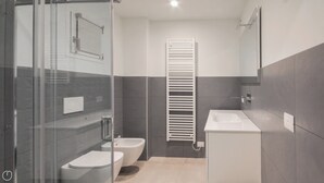 Un baño moderno con cabina de ducha de vidrio, inodoro, bidé, lavabo y toallero.