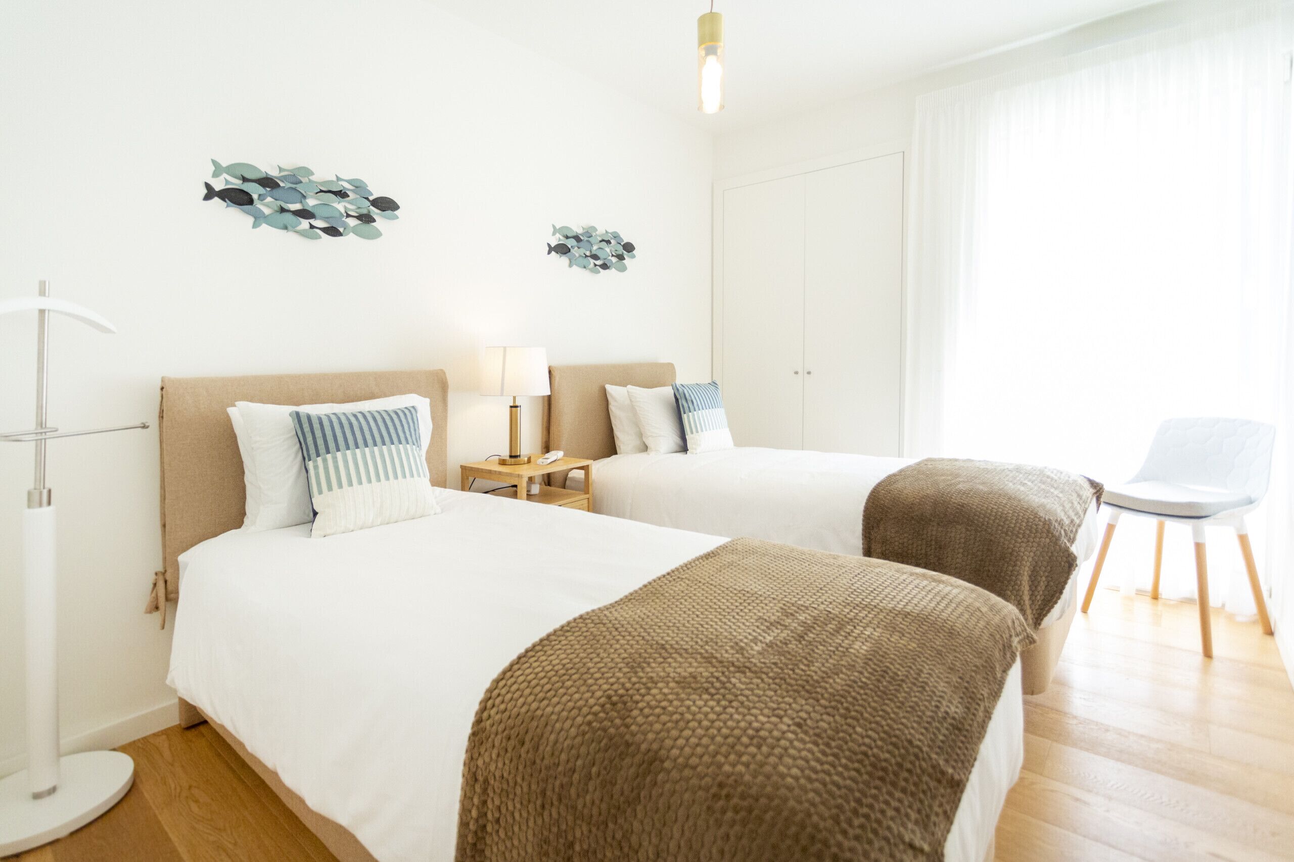 Une chambre d’hôtel avec deux lits, une table de chevet avec une lampe, une chaise et des œuvres d’art décoratives au mur.