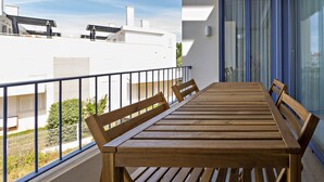 A balcony with a wooden table and chairs, a railing, and a view of neighboring buildings. - Modern, ideal for families (Cabanas de tavira)