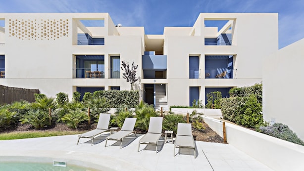 A modern building with a pool area, lounge chairs, and a staircase leading to the upper floors.
