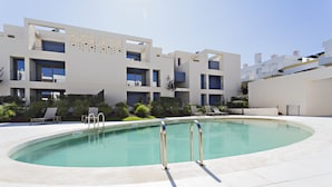 A modern hotel with a swimming pool, multiple balconies, and a landscaped garden area.