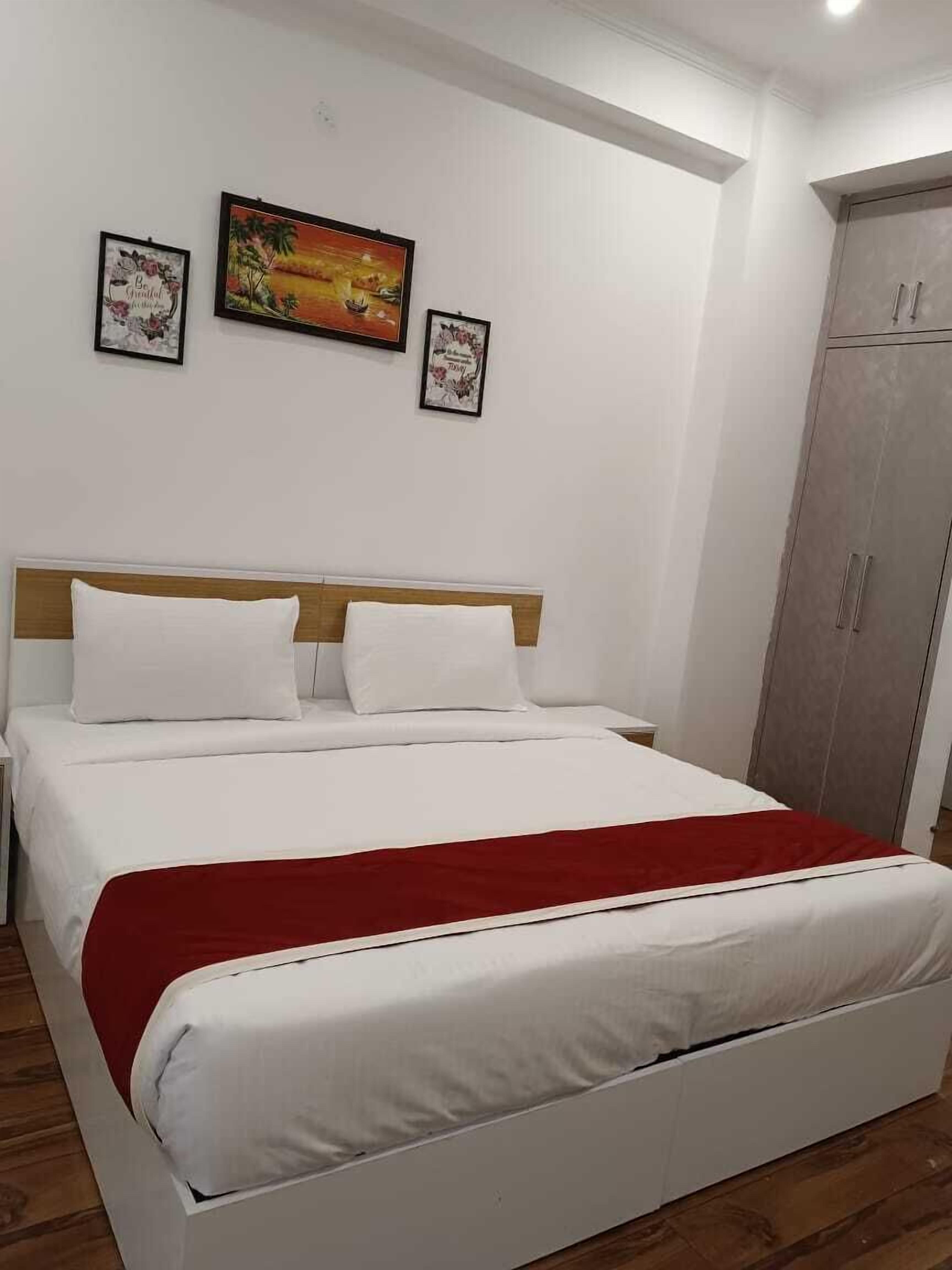 A bedroom with a bed, white bedding, a red throw blanket, and two framed pictures on the wall.