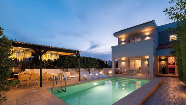 Un área de piscina moderna al aire libre con una pérgola, sillones de descanso y un patio bien iluminado.