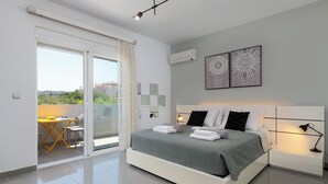 Un dormitorio moderno con cama, mesitas de noche, un escritorio con sillas y un balcón.