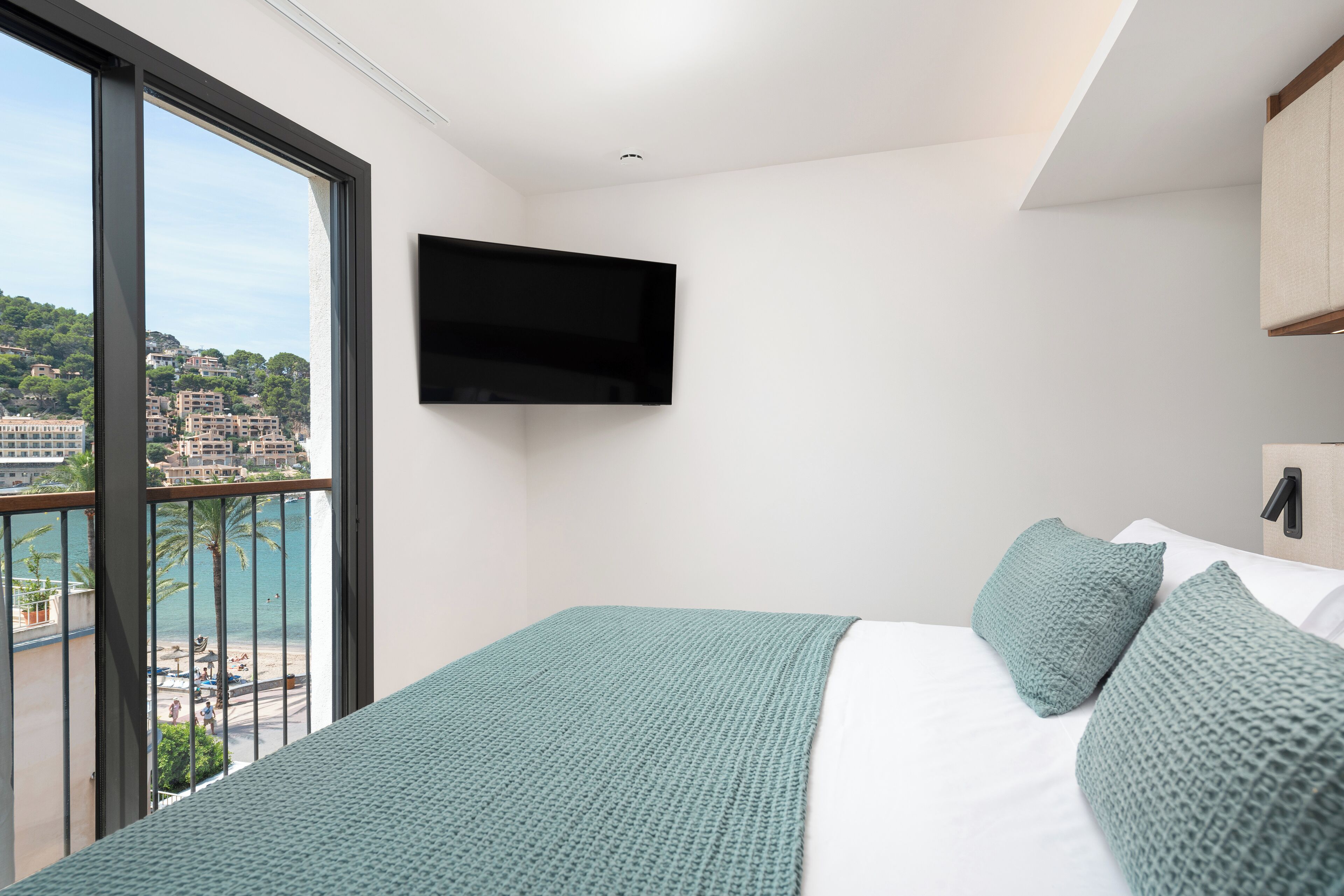 A bedroom with a large window, a bed with green bedding, and a mounted TV.
