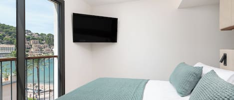 A bedroom with a large window, a bed with green bedding, and a mounted TV.