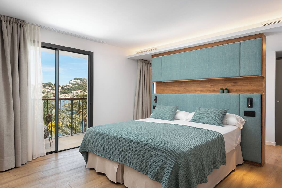A bedroom with a large bed, a view of the city, and a balcony.