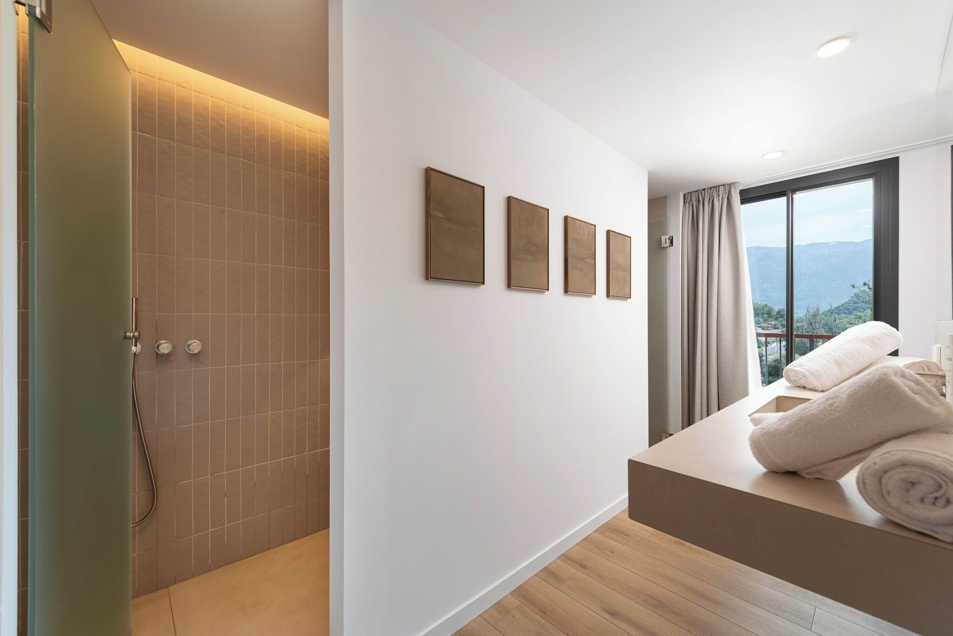 Un baño moderno con ducha, bañera y tocador con toallas. Hay cuatro cuadros enmarcados en la pared y un ventanal con vistas.