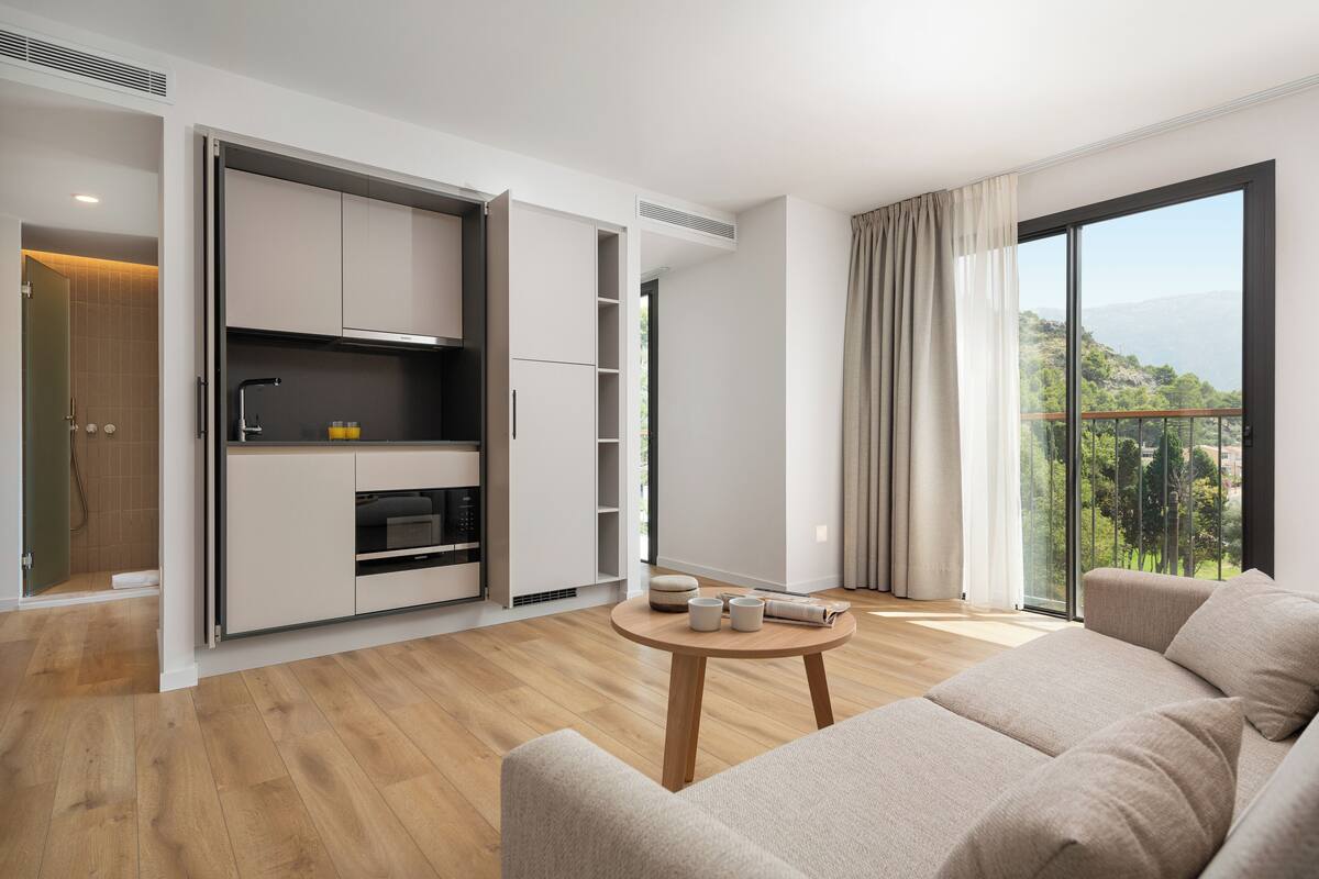 A modern living room with a sofa, a round wooden coffee table, and a kitchen area with cabinets and a built-in oven.