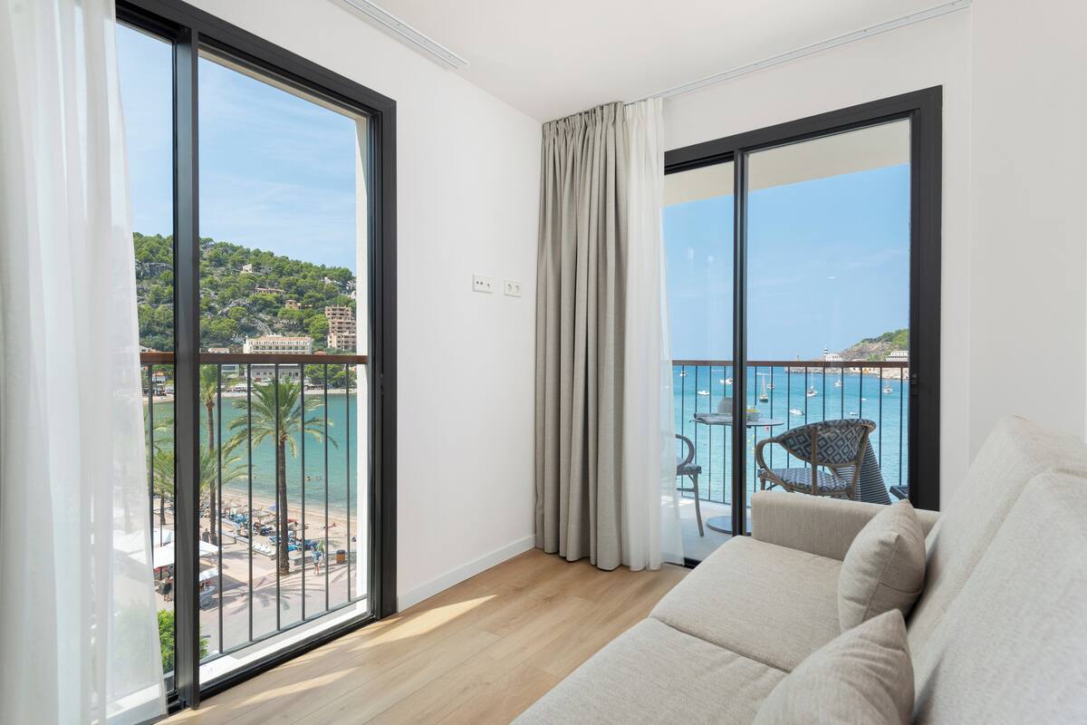 A balcony with a view of a beach and boats, a sofa, and a chair.