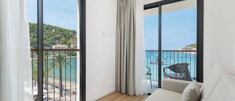 A balcony with a view of a beach and boats, a sofa, and a chair.