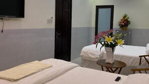 Een hotelkamer met twee bedden, een aan de muur bevestigde televisie, een klein tafeltje met een bloevas, en een airconditioner.