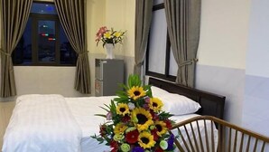 Een hotelkamer met een bed, een tafeltje met bloemen, een bankje en een raam met gordijnen.