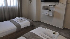 A hotel room with two beds, a TV mounted on the wall, and a small shelf with items. - Zennova 60 Nikiti Family Apt (Sithonia)