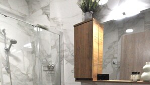A bathroom with a glass shower enclosure, a marble-tiled wall, a wooden vanity with a sink, and a mirror above the vanity. - Zennova 60 Nikiti Family Apt (Sithonia)