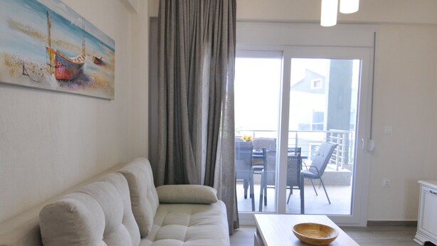 A modern living room with a sofa, a coffee table, and a painting on the wall. - Zennova 60 Nikiti Family Apt (Sithonia)