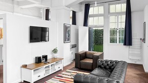 A modern living room with a black leather sofa, a white entertainment unit with a TV, and a colorful striped rug. - Maison Marvel l Enormous Loft Apt l Heart of City (Auckland)