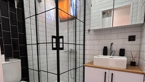 A modern bathroom with a glass-enclosed shower, a white toilet, and a wooden vanity with a sink. - Era House (Marmaris)