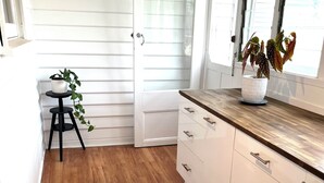 Una cocina con suelo de madera, armarios blancos y un ventanal con persianas.