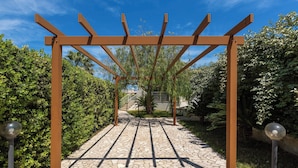 Una estructura de pérgola con un sendero de piedra que la atraviesa, rodeada de follaje.