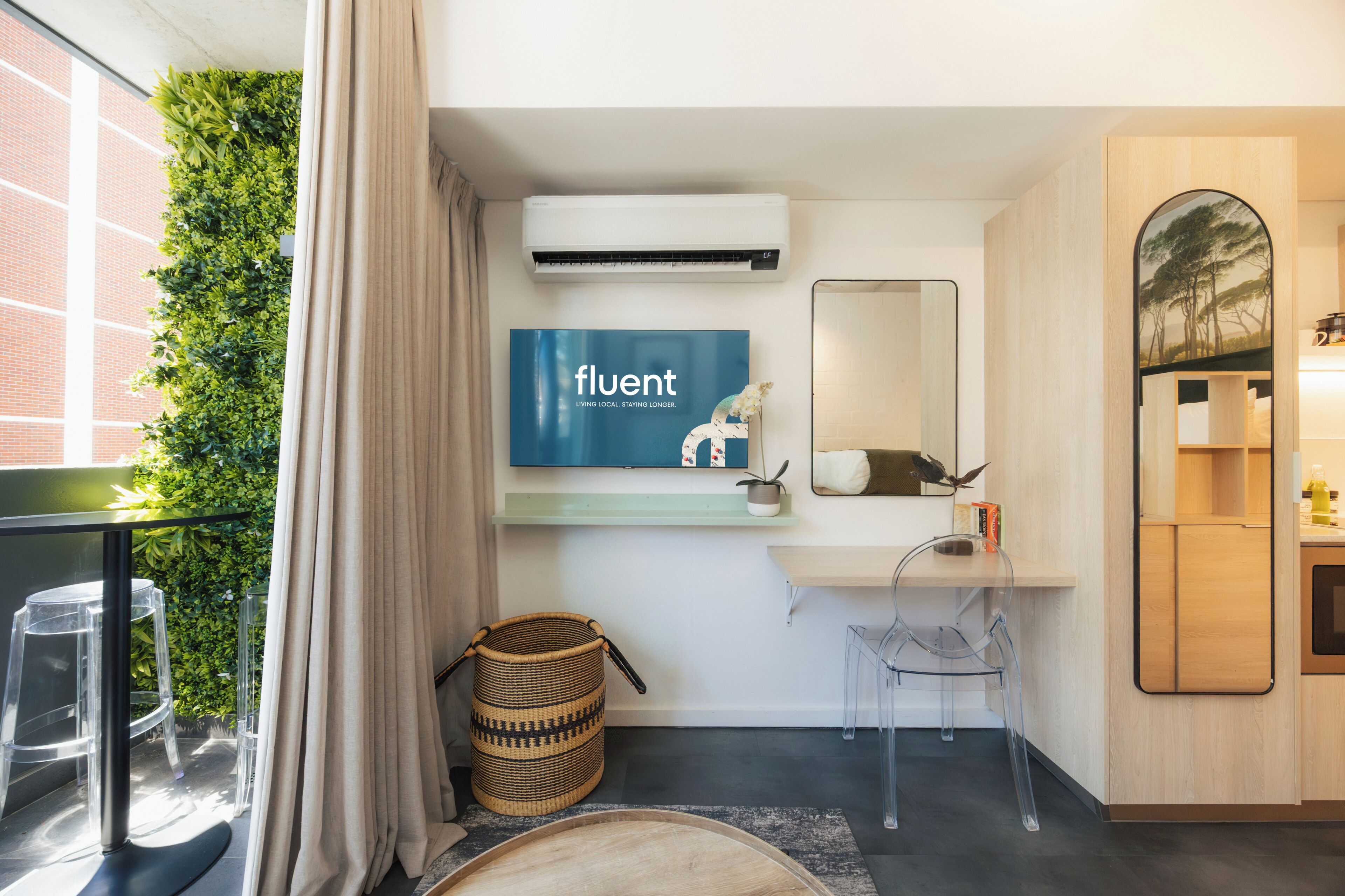 Un baño moderno con aire acondicionado instalado en la pared, un lavabo con espejo, un televisor fijado a la pared y una pared cubierta de plantas verdes.