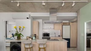 A modern kitchen with a central island, bar stools, a washing machine, and a microwave. - ONE26 ON M - Fluent Serviced Apartments (Cape Town)