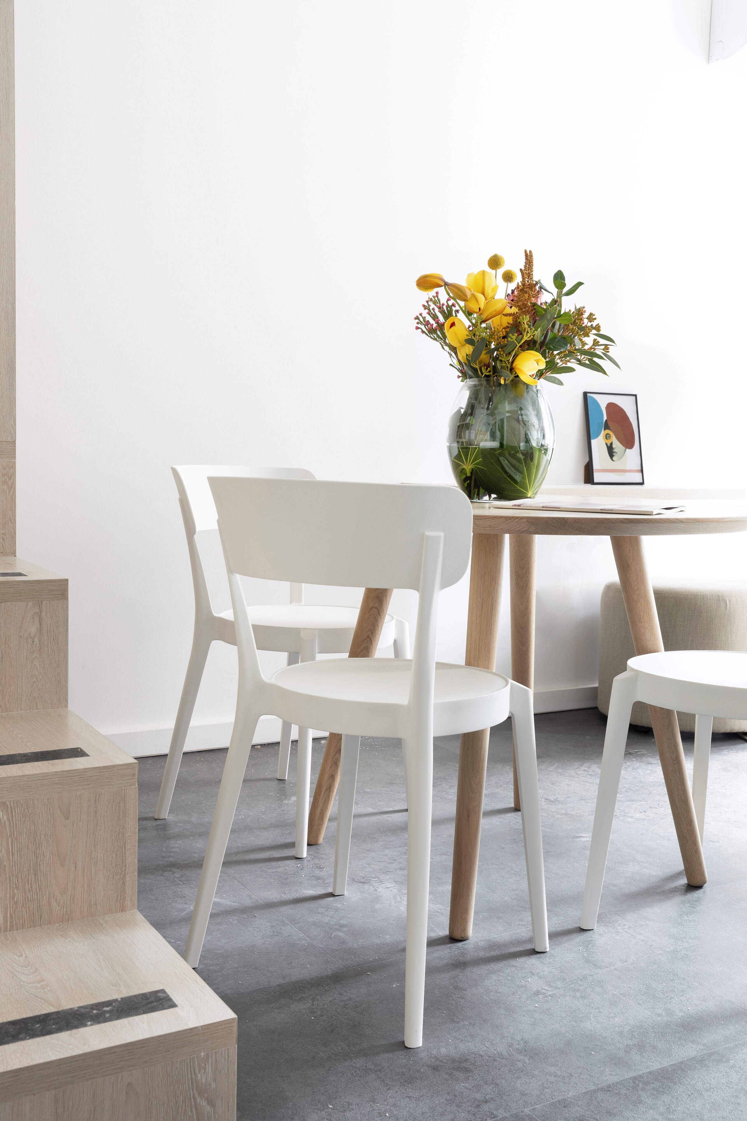 Un intérieur moderne avec une table blanche, des chaises et un vase rempli de fleurs jaunes.