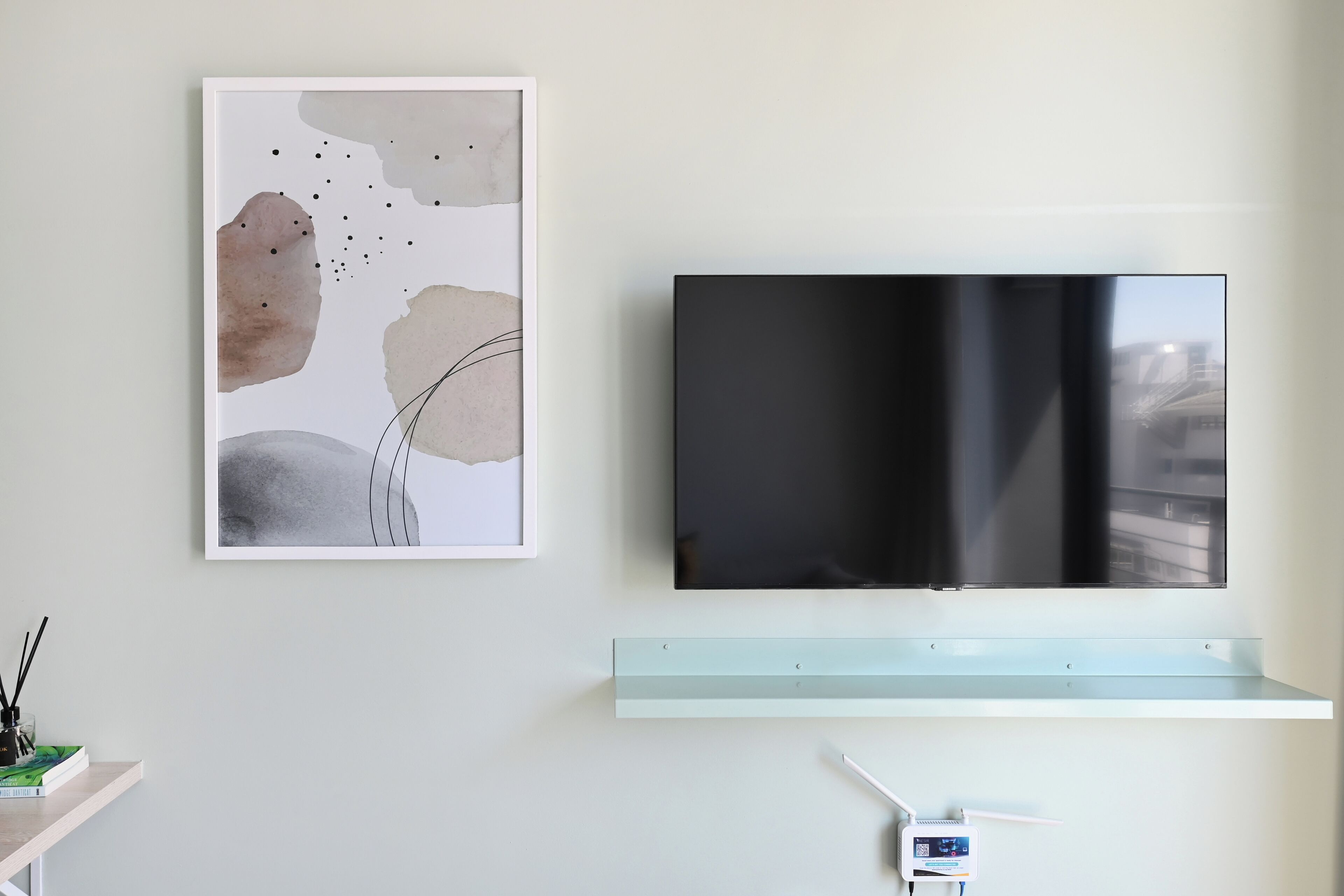A modern living room with a flat-screen TV mounted on a wall, a minimalist shelf below, and a framed abstract painting.