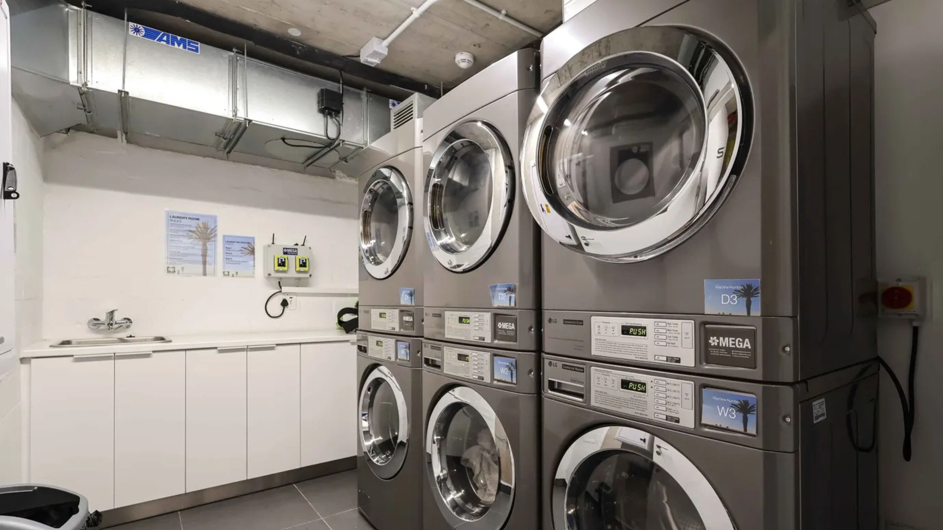 A laundry facility with multiple washing machines, a sink, and a wall-mounted fire alarm.