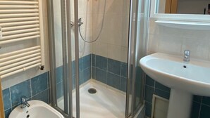 Un bagno con doccia vetrata, lavabo su piedistallo, bidet e specchio sopra il lavabo.