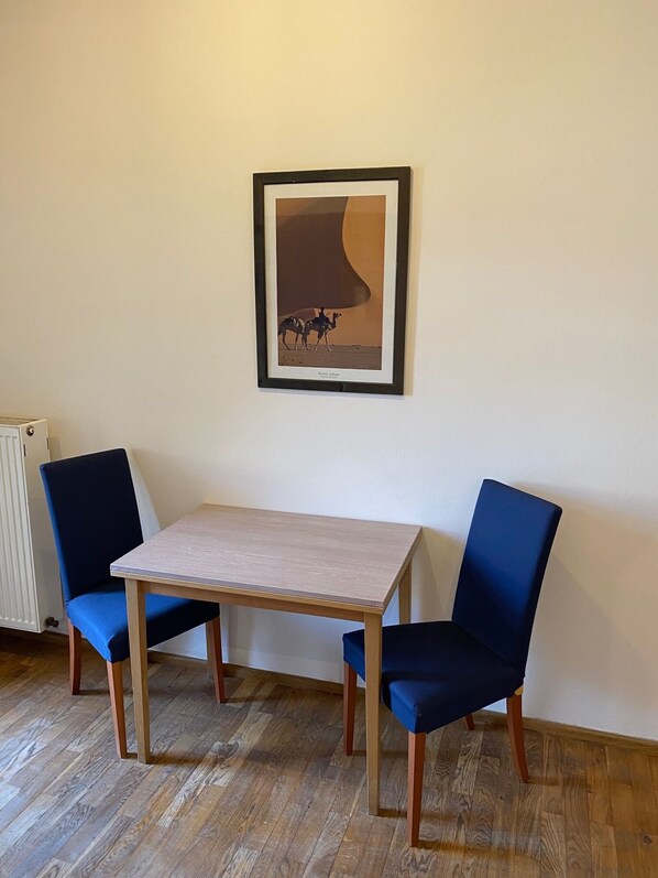 Una habitación con una mesa, dos sillas, un cuadro en la pared y un radiador.